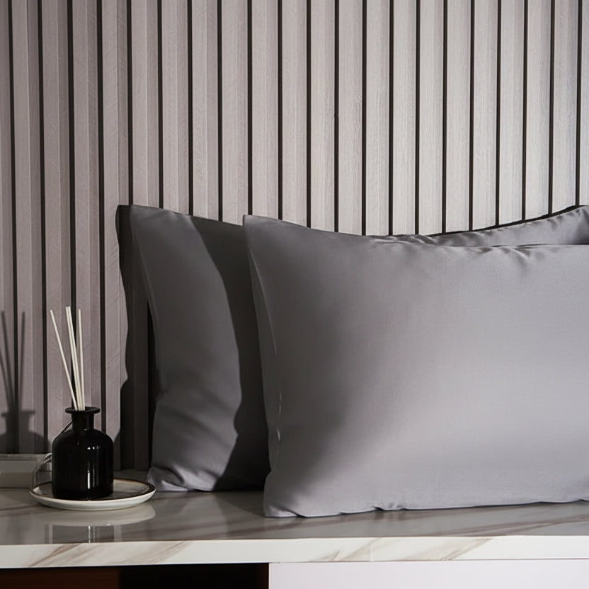 Gray satin pillowcases on a marble surface with striped wallpaper in the background