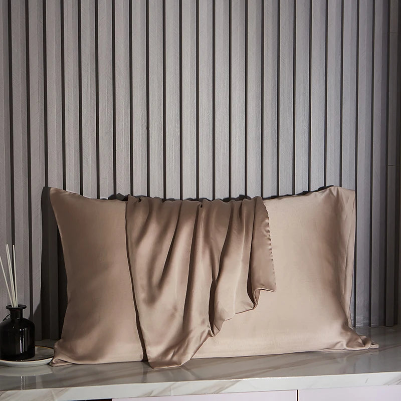 Khaki satin pillowcases on a marble surface with striped wall in the background