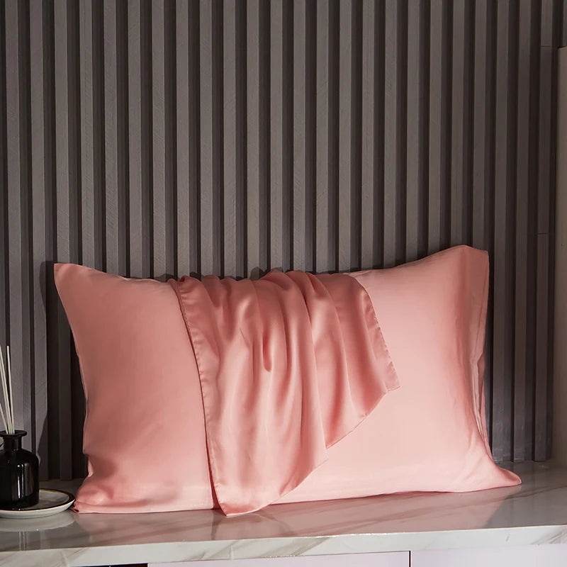 Pink satin pillowcases on a marble surface with a striped wall in the background