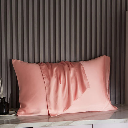 Pink satin pillowcases on a marble surface with a striped wall in the background