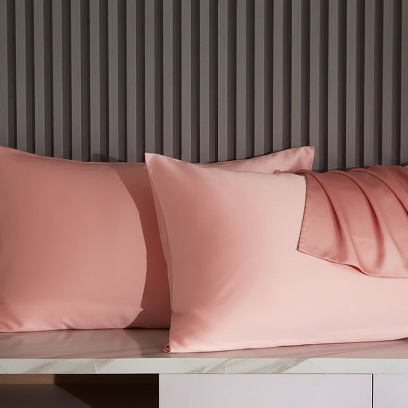 Pink satin pillowcases on a marble surface with a striped wall in the background