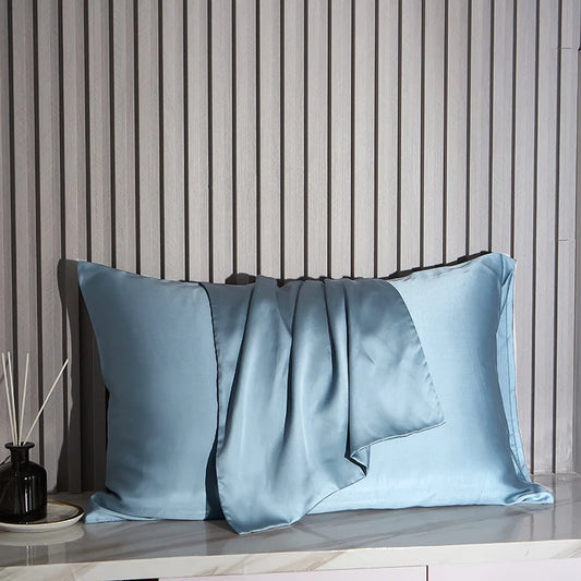 Blue satin pillowcases on a wooden surface with a striped wall background