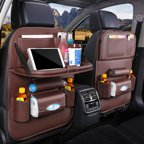 Car backseat organizer with multiple pockets holding a tablet, drinks, and snacks with a scenic view outside.