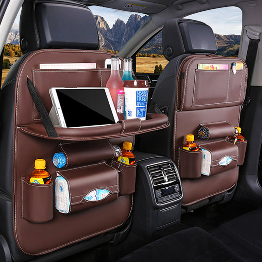 Car backseat organizer with multiple pockets holding a tablet, drinks, and snacks with a scenic view outside.