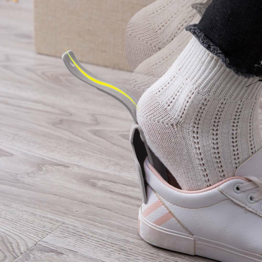 Close-up of a person wearing a white sneaker with a yellow sole on a wooden floor.