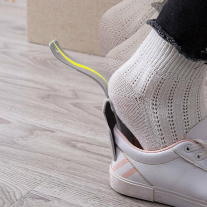 Close-up of a person wearing a white sneaker with a yellow sole on a wooden floor.