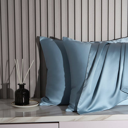Light blue satin pillowcases on a wooden surface with a striped wall background