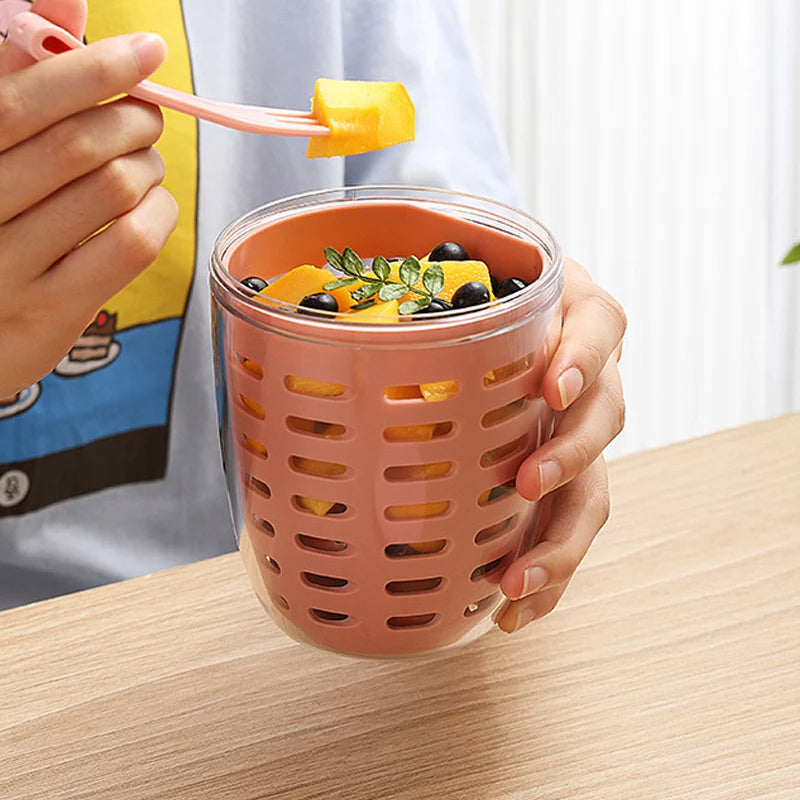 Person holding a pink mesh cup filled with fruit on a wooden table.