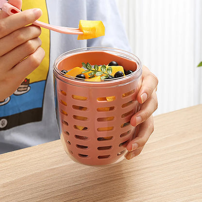 Person holding a pink mesh cup filled with fruit on a wooden table.