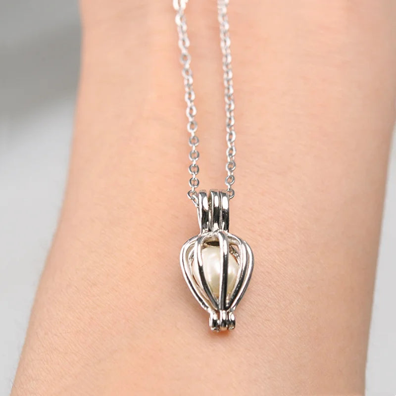 Silver hot air balloon pendant necklace on a person's wrist against a neutral background