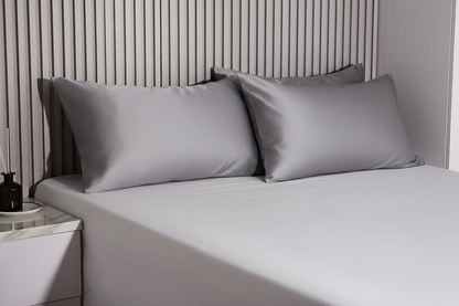 3 Gray satin pillows on a bed, striped wallpaper in the background