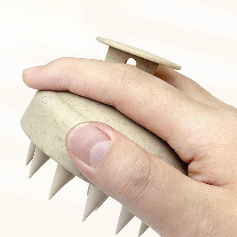 Hand holding a beige scalp massager with a white background
