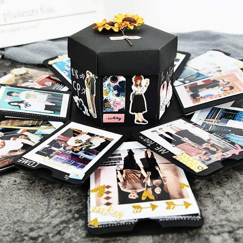 Black hexagonal photo album with cut-out decorative elements on a surface with scattered photos.