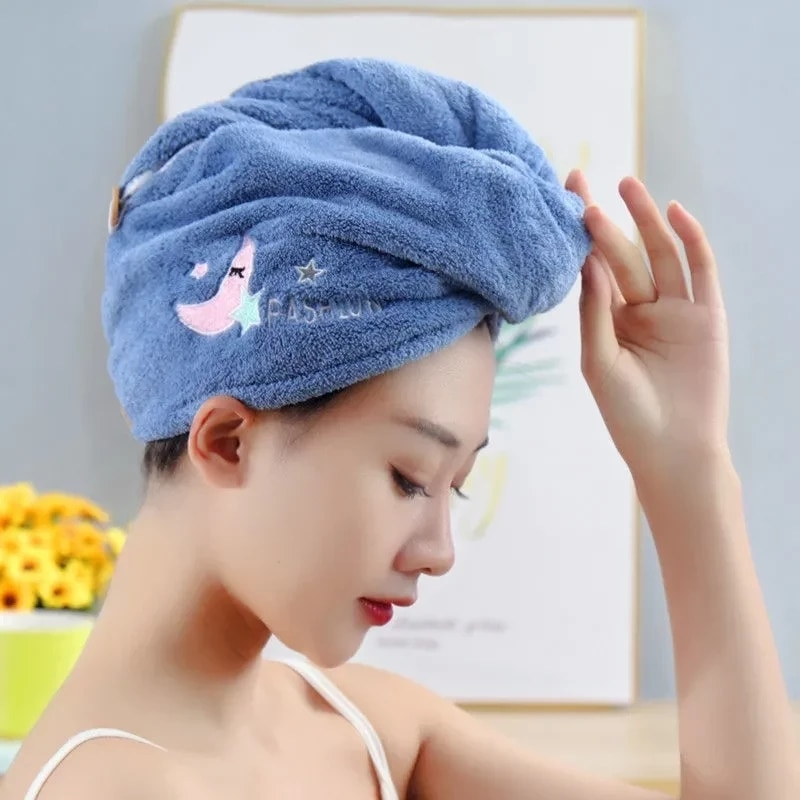 Woman wearing a blue hair towel with cartoon designs, holding it above her head.