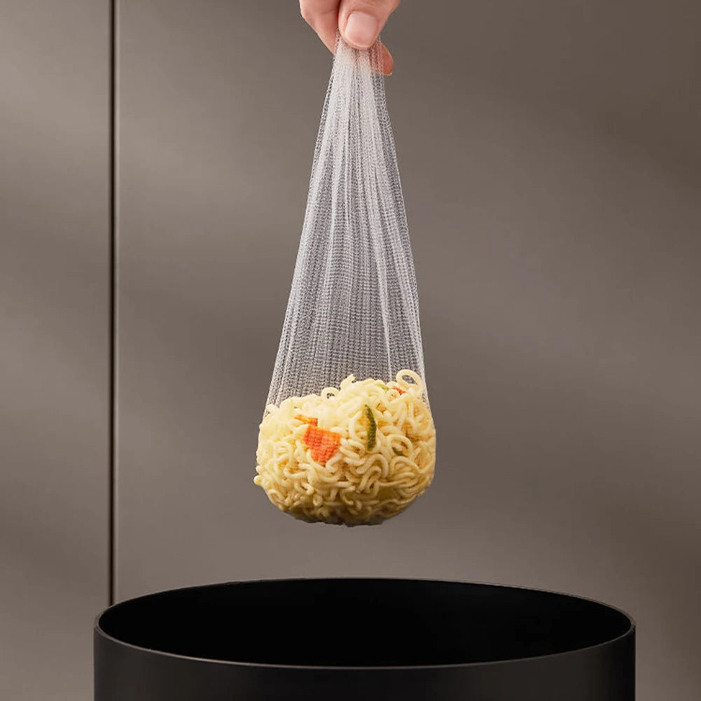 Hand holding a mesh bag with noodles over a black trash can against a gray background