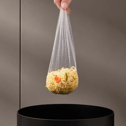 Hand holding a mesh bag with noodles over a black trash can against a gray background