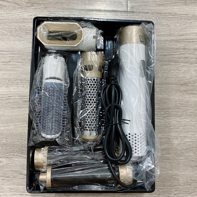 Set of grooming tools including a hair dryer, attachments, and a cable in a black plastic packaging on a wooden surface.