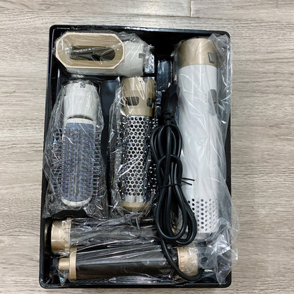 Set of grooming tools including a hair dryer, attachments, and a cable in a black plastic packaging on a wooden surface.