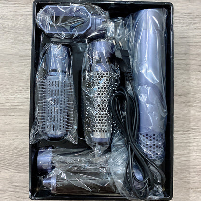 Set of hair styling tools including a hair dryer, brush, and attachments in clear plastic packaging on a wooden surface.
