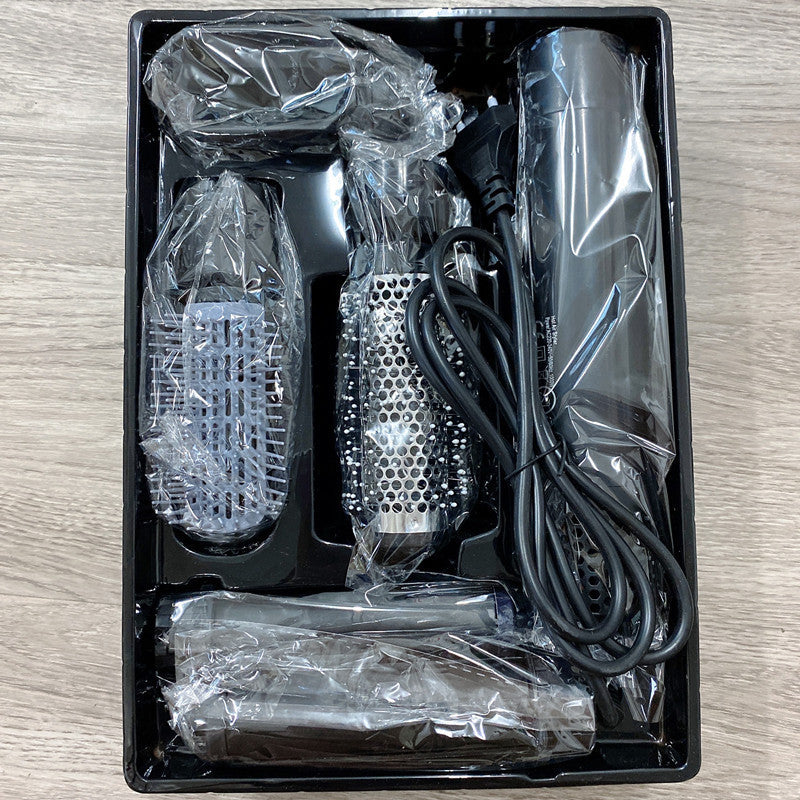 Grooming kit with hair dryer, brush, and attachments in a black box on a wooden surface.