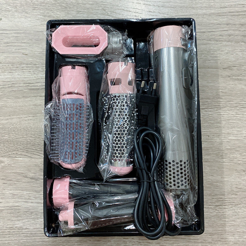 Grooming tool set with pink and silver components in clear plastic packaging on a wooden surface.