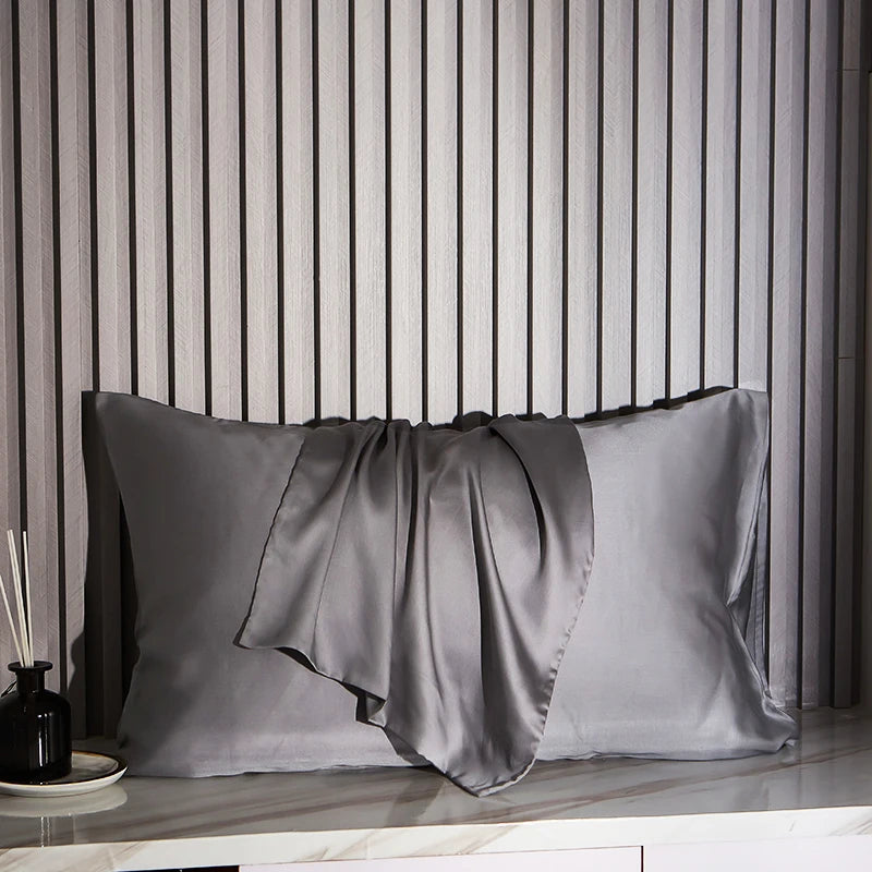 Dark Gray satin pillowcases on a marble surface with striped wallpaper in the background