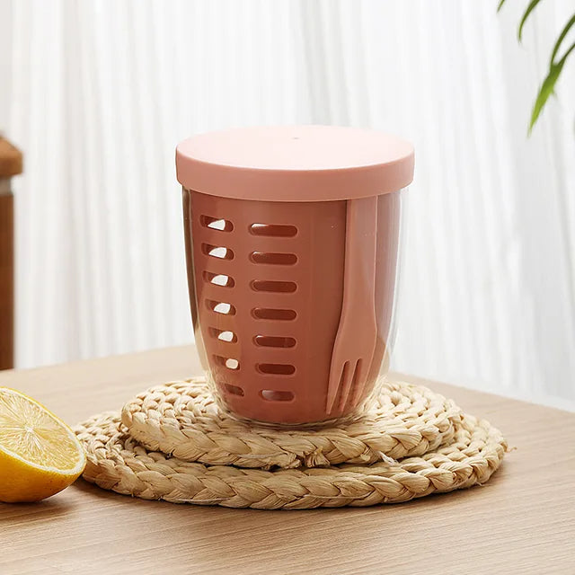 Pink kitchen utensil holder on a woven mat with a lemon on a wooden surface.